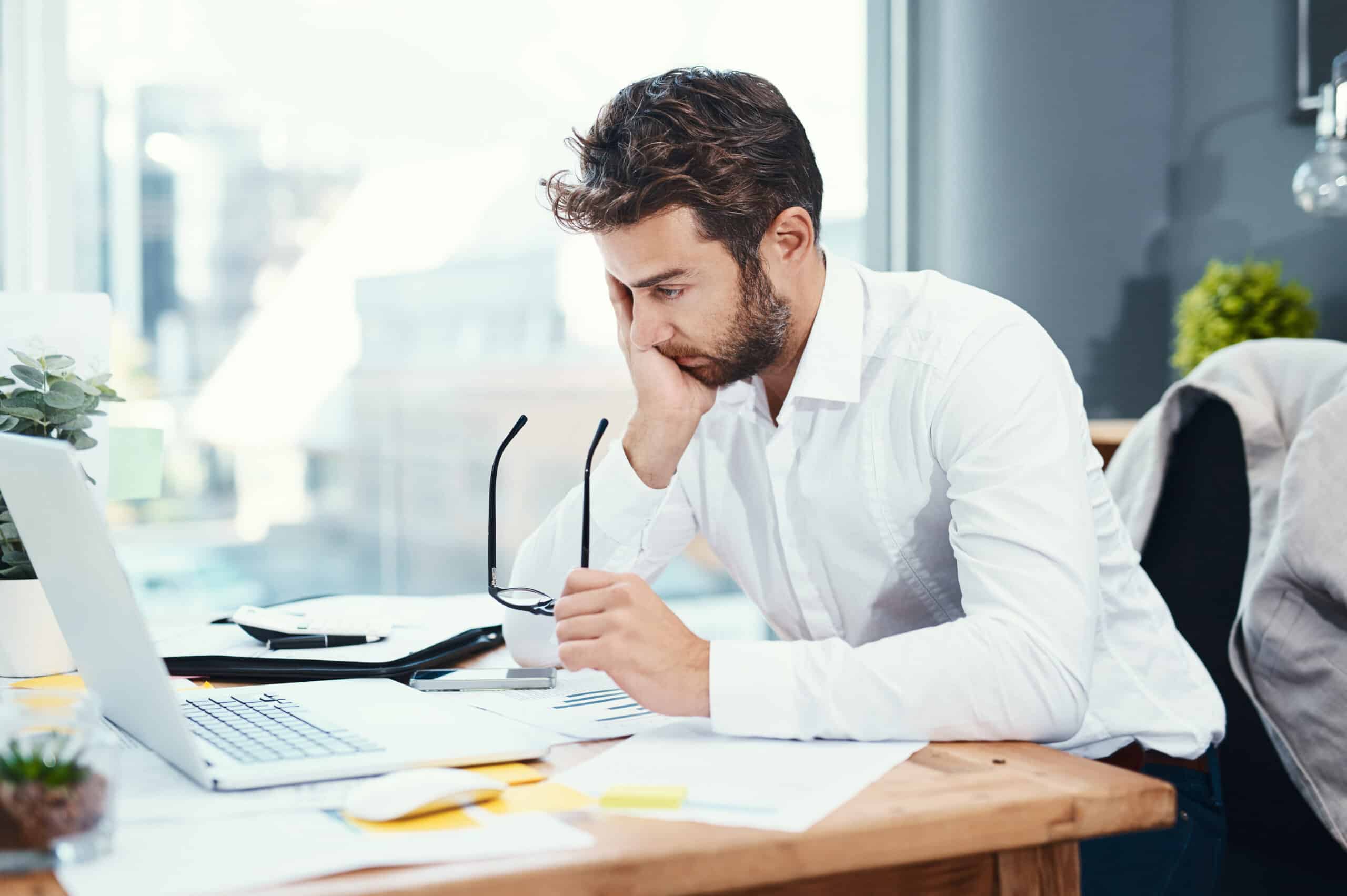 Office, laptop and man with headache by desk for tension, pain and brain fog in accounting job. Finance, business and frustrated with glasses by tech for audit information, mistake and digital review
