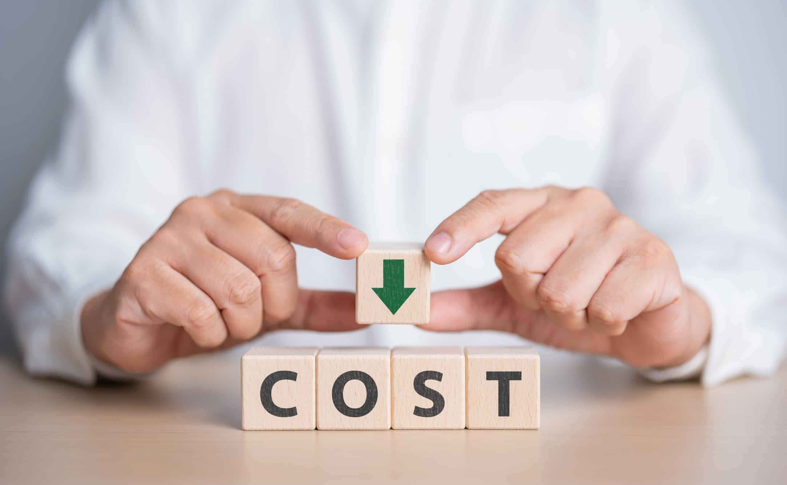 Businessman's hands hold wooden cube with a green arrow down and COST word. Lean optimize manufacturing. Decreasing company expense to maximize profits. Business process improvement to reduce cost.